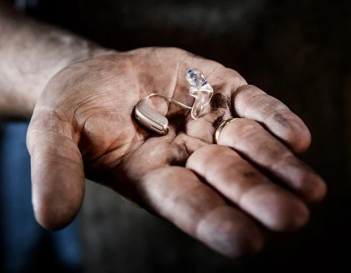 Eine Hand hält ein modernes Hörgerät zur Unterstützung bei Hörverlust und Schwerhörigkeit.