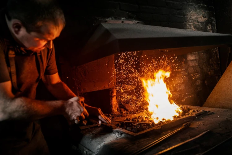 Ein Schmied arbeitet in einer traditionellen Schmiede am offenen Feuer mit Funkenflug.