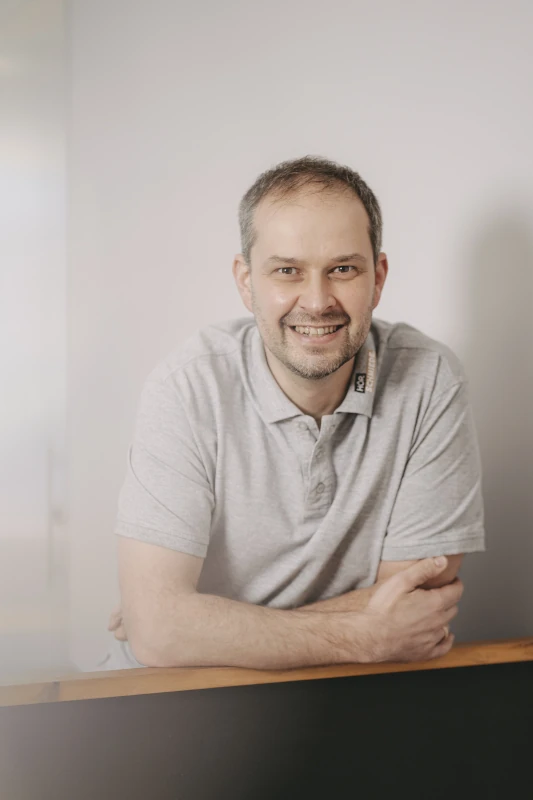 Mann mit grauem Poloshirt lächelt freundlich in modernem Büro vor neutralem Hintergrund.