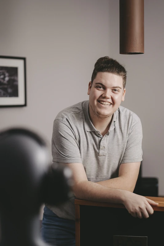 Junger Mann mit grauem Poloshirt lächelt freundlich in modernem, hellen Büro.